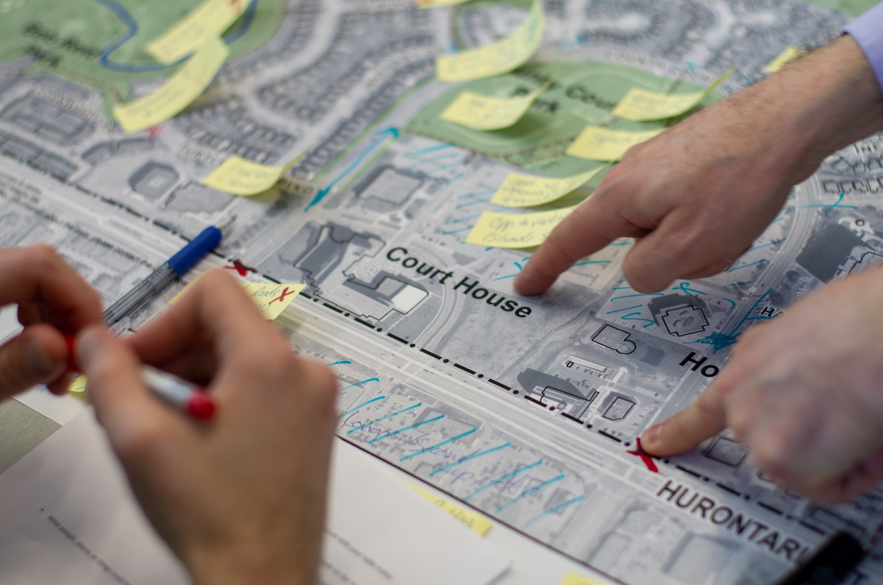 3 hands pointing and writing on a map of county court with sticky notes on it